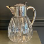 A Fine Quality Cold Duck Jug, 20th Century Colorless glass, peeled, star base, silver-plated metal mount with spout, hinged lid, and handle, glass insert for ice cubes, height approx. 26.5 cm, rubbed, stained