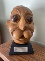 This is a wood carving titled “Esky,” produced by Esquire Inc. in 1948, representing the whimsical mascot head associated with the magazine. The sculpture exudes a playful, cartoonish character with exaggerated facial features, including prominent, bulging eyes and a comically oversized nose and mouth. The craftsmanship is evident in the smooth contours and the rich patina of the wood, which may suggest a variety of hardwood. Mounted on a black base with a plaque, this piece captures the humor and bold style of post-war American pop culture. Display figure for department stores or specialty stores  designer Elmer Simms Campbell